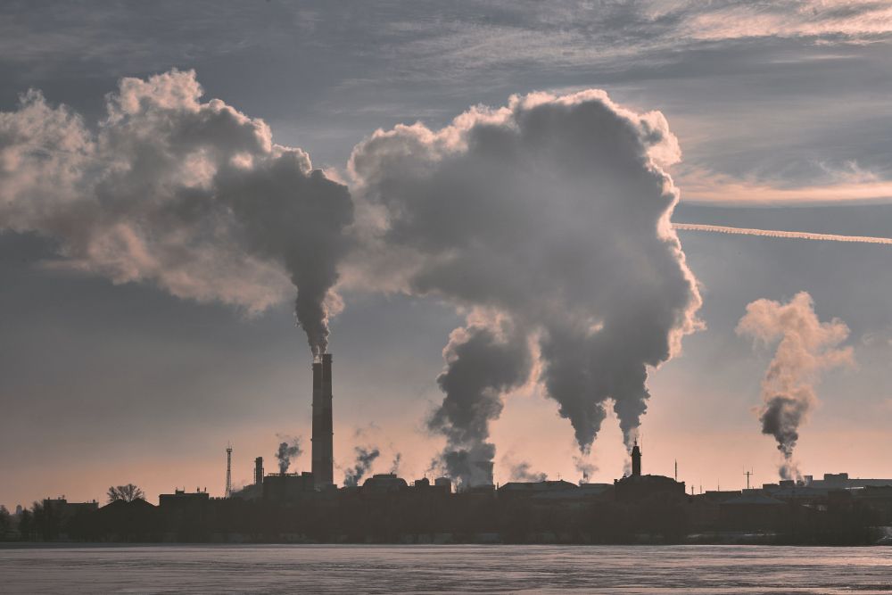 Factory chimneys pumping out clouds of emissions into the air next to water.
