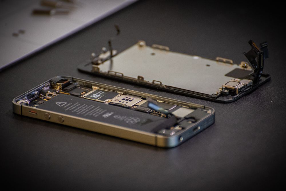 Smartphone with screen removed and inner components exposed resting on dark surface.